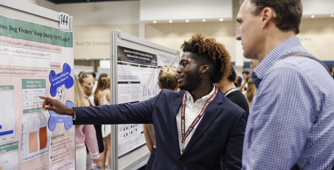 An undergraduate student points to his poster as he explains his project to a reviewer at Discover USC 2024,