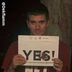 Image provided by @Dekflamm_ of a young man smiling and holding an acceptance envelope beneath his chin that says, Yes!