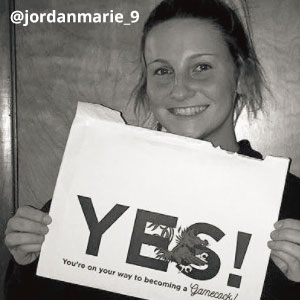 Black-and-white image of @jordanmarie_9 smiling and holding an acceptance envelope under her chin that says, Yes!