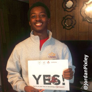 Image provided by @JordanPixley of a young man wearing a pullover and smiling while he holds an acceptance envelope in front of his chest that says, Yes!