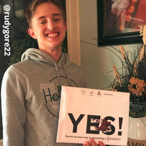 Image provided by @rudygore22 of a young, blonde, man smiling broadly and holding an acceptance envelope that says, Yes!