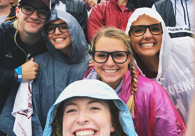 Group of students wearing glasses in rain at football game.