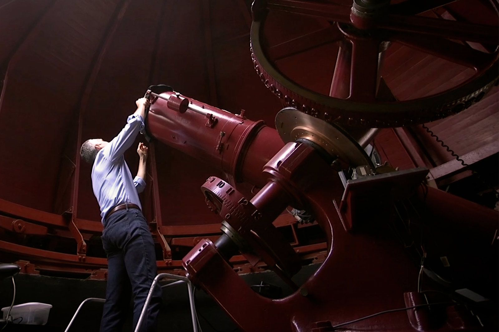 The back of someone in the domed room of the Melton Observatory reaching up to adjust the telescope.