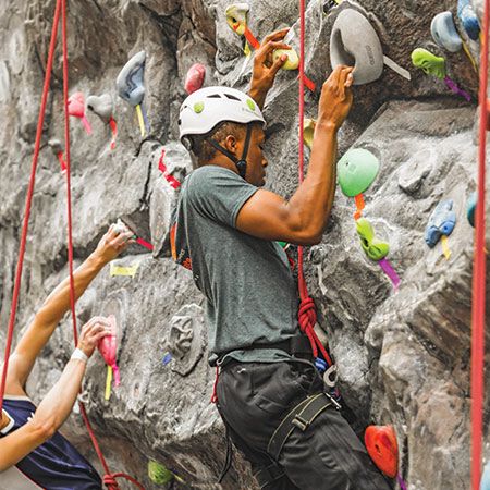 Student wearing a helmet and harness climbing a rock wall.