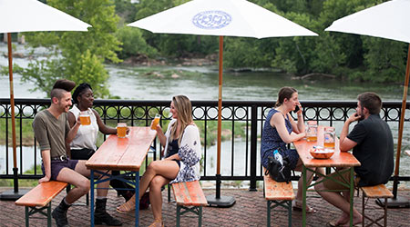 People sitting at outdoor tables with umbrellas looking over the river. 