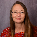 Jennifer Reynolds has fair skin, long brown hair, oval-shaped glasses and wears a red patterned blouse. 