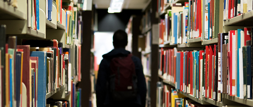 a student walks down between two shelves in a library.