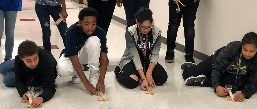 students test out popsicle stick creations in the hallway