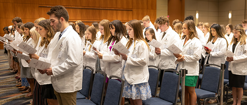 Group of students in white coats reciting a pledge