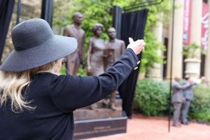 woman salutes during alma mater with a sculpture in the background