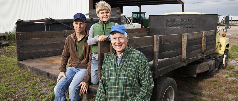 Three generations of male farmers posing outside with their work truck on a farm.