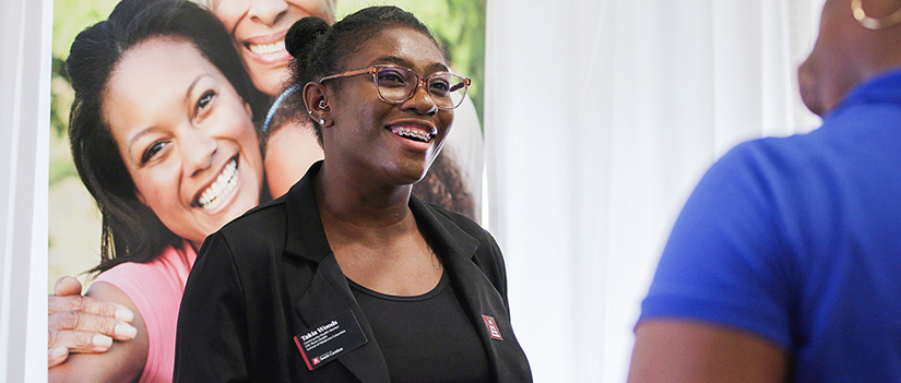 Image of a woman smiling and speaking to someone at a health fair. 