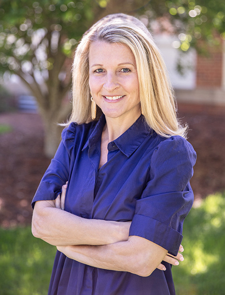 Image of a woman outside smiling at the camera with her arms crossed.