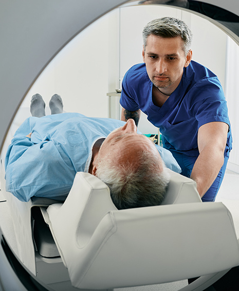 A patient is lying down and being placed into a MRI imaging machine by a medical technician who is standing next to him. 