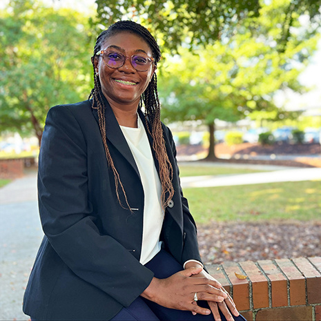 Headshot of Takia Woods seated on a brick wall outdoors.