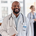 Image of a medical professional in a white lab coat holding a clipboard smiling.