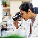 Image of a medical professinal in a lab coat looking through a microscope.