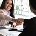 Image of a woman at at desk shaking another person's hand.