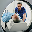 Image of an MRI machine with a patient lying down about to go into the machine with a medical professinal assisting him.