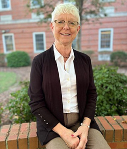 Headshot of Kathie Janssen outdoors sitting on a brick wall. 