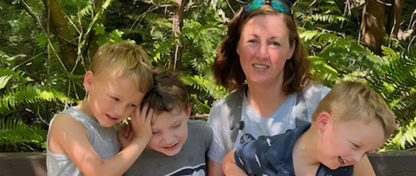 Kate Bowman smiles at the camera while surrounded by her three young sons.