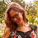 Bri Ash, a white woman with long brown hair, smiles in front of greenery