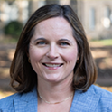 Dr. Lindsay McCary, a white woman with shoulder length brown hair, smiles at the camera for a professional headshot on the Horseshoe.