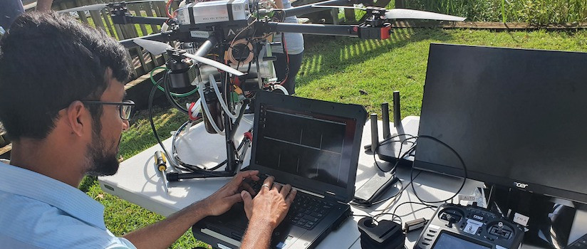 A researcher works on-site at Lake Wateree with water quality measuring equipment and drone water sampler on a table in front of them