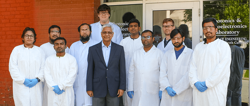 Several people in lab jackets standing behind Dr. Asif Khan in front of a laboratory