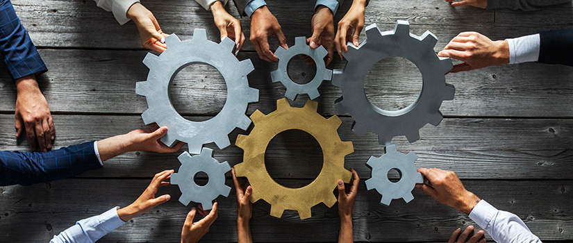 Hands holding gears together in place to symbolize a team working together similarly to a machine.
