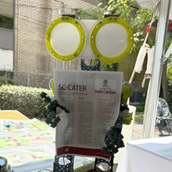 Small robot holding a flyer for SC-CATER