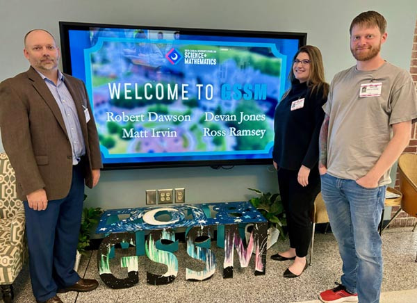 Three people standing in front of a screen that reads "Welcome to GSSM"