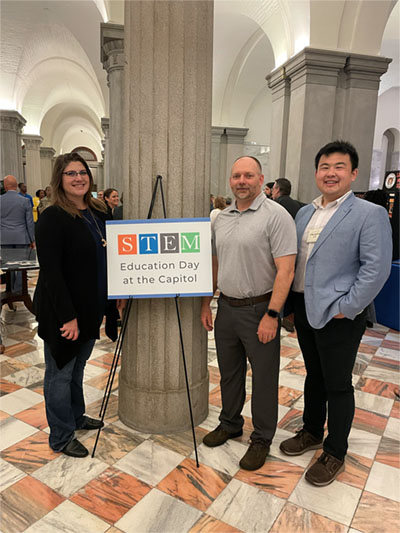Devan Jones, Matt Irvin, and Hengtao Tang standing around a sign that reads "STEM Education Day at the Capitol."