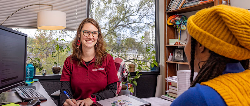 A white female advisor talks to a black female student. 
