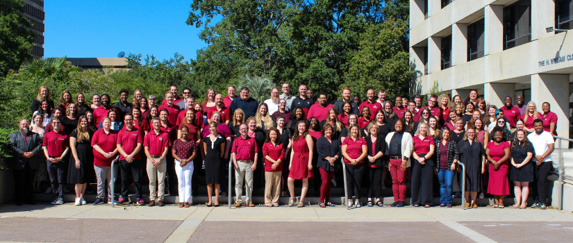 100+ staff wearing garnet and black stand on the steps of the Close Hipp building. They are all smiling at the camera. 