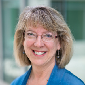Dr. Schreiner is pictured from the shoulders up wearing a blue blazer. She is wearing glasses and is smiling. 
