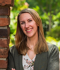 Lisa is pictured from the shoulders up wearing a green sweater. She has light skin, blonde hair and is smiling.