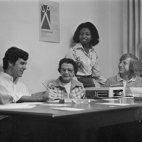 In this black and white photo, Ada Thomas is surrounded by student advisees. They are looking at a piece of paper on a table. 