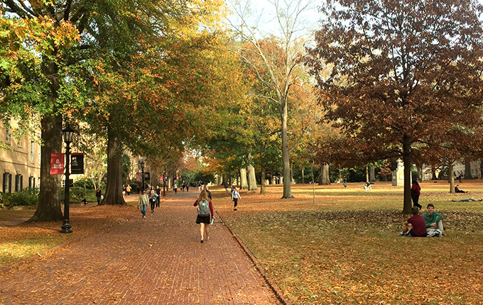 Students walking the brick walkways of the UofSC Horseshoe, surrounded by trees and historic buildings.