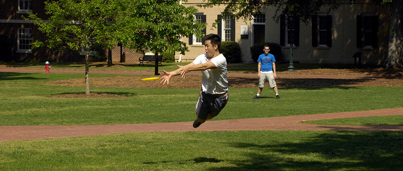 a male student flying through the air attempting to catch a frisbee on the Horseshoe