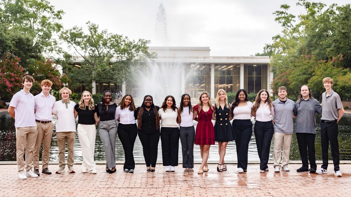 students celebrating by jumping up and down in front of the fountain outside the library