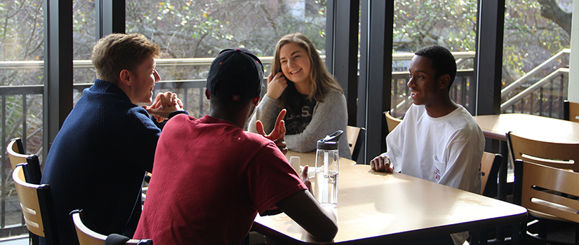 Students eating together beside a window.