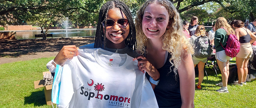 two girls holding a sophomore initiative t-shirt