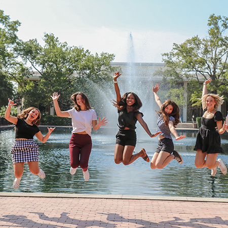 students jumping into the air in front of the fountain