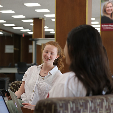 two students talking and sitting in the library