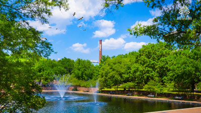 Thomas Cooper Fountain on a bright, sunny day with the smokestack in the background and tree and gates mark.