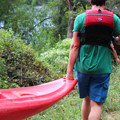 Student in a life vest carrying a red kayak.