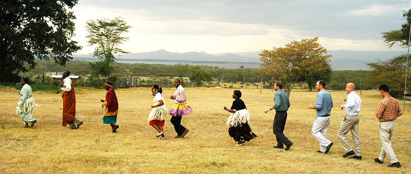 Volunteers and locals dancing in a circle on a field in Kenya. (Courtesy of Peace Corp)