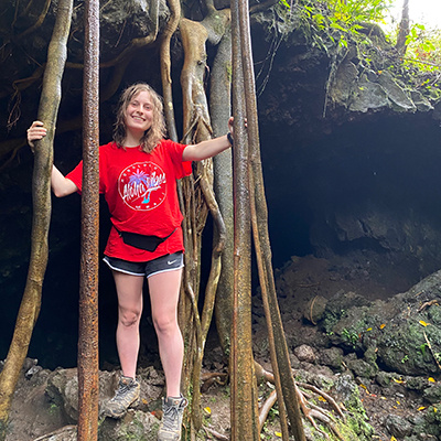 Lauren hanging onto tree roots outside of a hidden cave in Hawaii