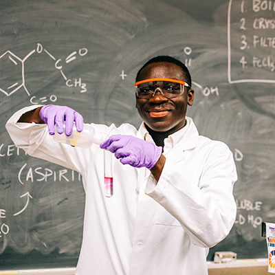 Kwame doing an experiment in a lab coat and goggles